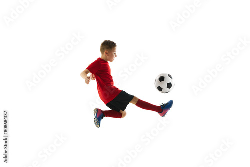 Dynamic portrait of sportive child, boy in red uniform playing, training football against white studio background. Concept of professional sport, championship, youth league, hobby. Ad