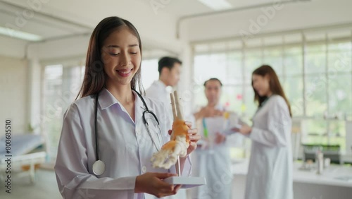 Portrait of young asian woman orthopedist doctor in uniform holding human ankle bone skeleton model, smiling to camera at hospital. Medical orthopedist photo