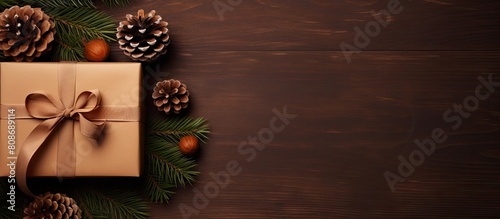 Top view of a beautifully wrapped Christmas present adorned with pine cones and juniper branches placed on a brown background Ample copy space available