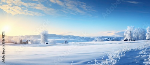A picturesque countryside scene with a sunny winter sunrise a snow covered field a valley and a clear blue sky The bright light illuminates the panoramic view creating an idyllic and peaceful atmosph