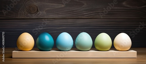 The wooden surface hosts a carton of speckled Easter eggs consisting of six pastel colored shades of yellow green and blue The image features copy space on the right side