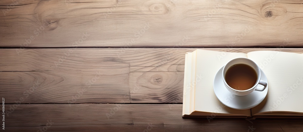 Top view of a wooden table with an open book featuring blank pages accompanied by a cup of tea The image provides ample copy space for adding text or graphics Top view of a wooden table with an open book featuring blank pages accompanied by a cup of tea The image provides ample copy space for adding text or graphics