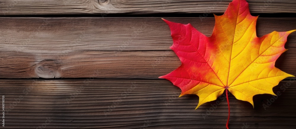 Obraz premium A handmade maple leaf crafted from yellow and red paper stands out against a rustic wooden background symbolizing the arrival of autumn It is a representation of children s DIY crafts and welcomes th