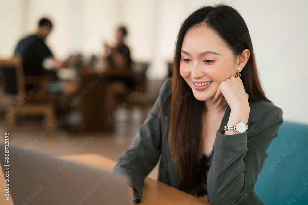 Business concept, Smiling professional young Asian businesswoman Joyful woman working on her laptop in cafe setting. Business concept, Smiling professional young Asian businesswoman Joyful woman working on her laptop in cafe setting.