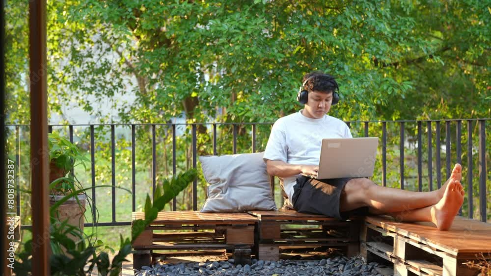 Asian man working on laptop computer with using AI browsing data at home. Male freelance sitting at balcony and working online corporate business. Modern life and remote working technology concept. Asian man working on laptop computer with using AI browsing data at home. Male freelance sitting at balcony and working online corporate business. Modern life and remote working technology concept.