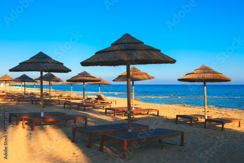 Exotic sunbeds and umbrellas on the sandy beach. Tropical coast with sun loungers 
