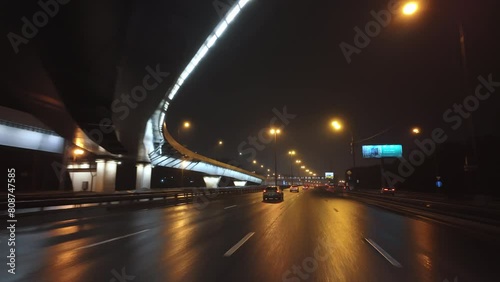 Driving a car at night in illuminated rainy city streets, windshield view