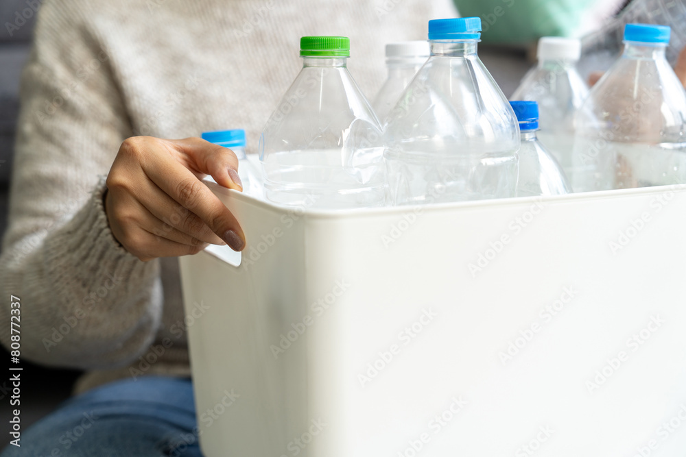 Φωτογραφία A woman wearing a cream sweater collects and sorts recycled plastic bottles into white trash cans in a living room