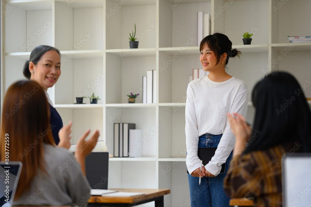 Smiling Asian student woman having presentation while her classmates giving applause Smiling Asian student woman having presentation while her classmates giving applause