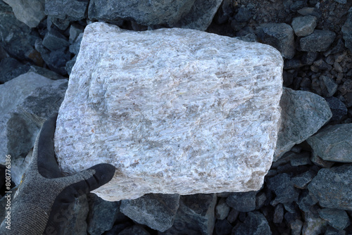 Photos Hand, protective glove, large pegmatite spodumene ore rock amongst waste (barren in lithium)