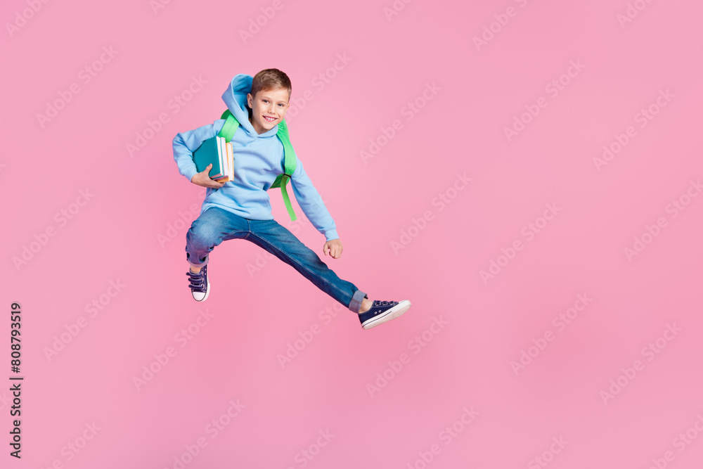 Full body portrait of energetic little schoolkid hold book backpack jump empty space isolated on pink color background