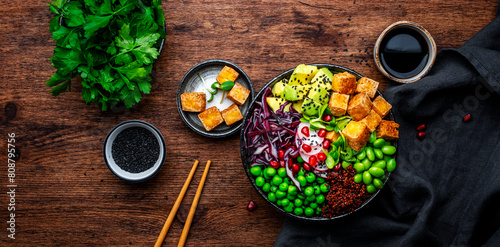 Vegan Buddha Bowl for balanced diet with tofu, quinoa, vegetables and legumes. Wooden table background, top view