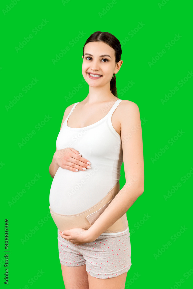 Portrait of elastic maternity band dressed on pregnant woman to reduce backache at green background with copy space. Orthopedic abdominal support belt concept Portrait of elastic maternity band dressed on pregnant woman to reduce backache at green background with copy space. Orthopedic abdominal support belt concept
