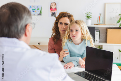 Young adult mother visiting pediatrician doctor with her little sick daughter at medical consultation room. Children healthcare concept.