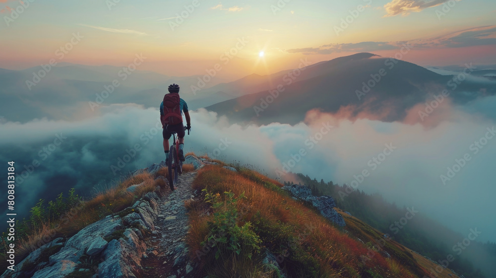 Determined cyclist on mountain trail at sunrise overlooking misty valley.