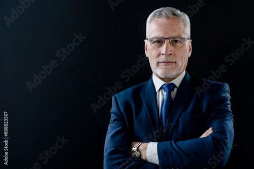 Portrait of mature businessman in suit and eyeglasses on black background. Close up headshot of confident good looking middle age leader, ceo male businessman looking at camera © InsideCreativeHouse