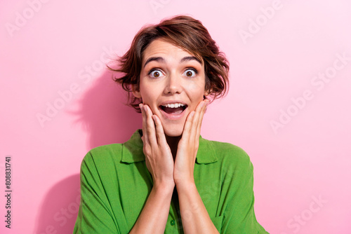 Photo of impressed shocked young woman dressed green shirt arms cheeks open mouth isolated pink color background