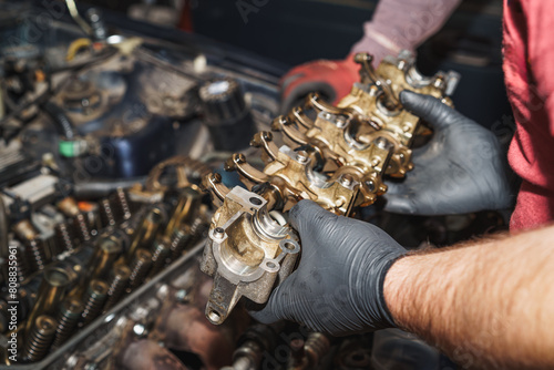 The mechanic is holding the rocker arm in his hand, which he will reinstall into the car engine. Auto service. Car repair. Workshop.