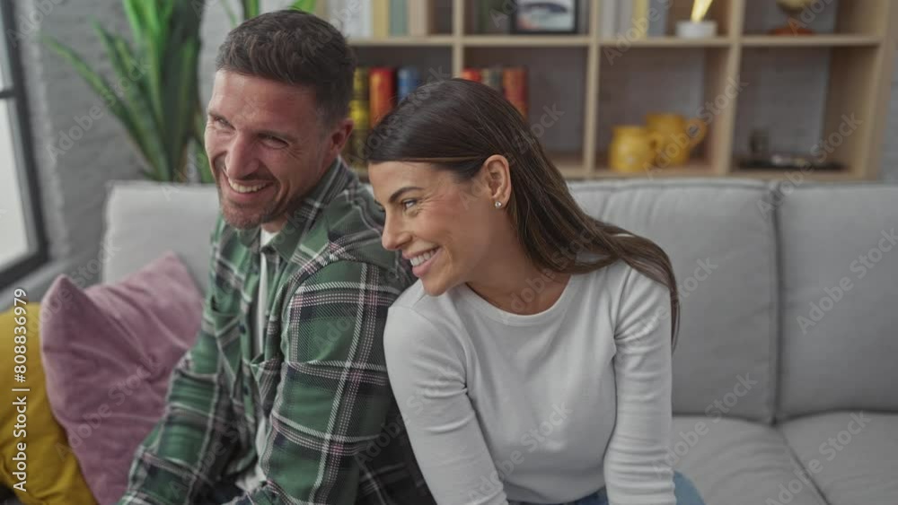 Laughing hispanic couple relaxing together on a cozy sofa in a modern living room Laughing hispanic couple relaxing together on a cozy sofa in a modern living room