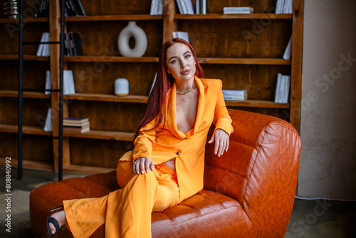 Red-haired girl in an orange business suit sitting on a leather sofa in the library