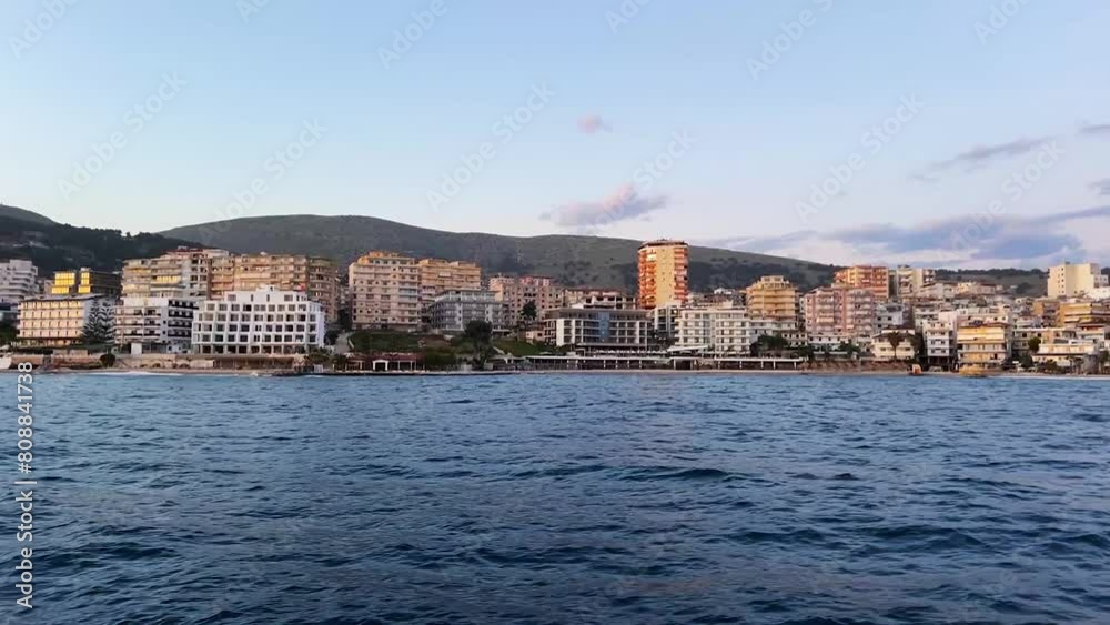 Savor the mesmerizing view of Sarandë from a sailing boat during the golden hour, as the sun sets over the horizon, casting a warm glow upon the tranquil waters and picturesque coastline Savor the mesmerizing view of Sarandë from a sailing boat during the golden hour, as the sun sets over the horizon, casting a warm glow upon the tranquil waters and picturesque coastline