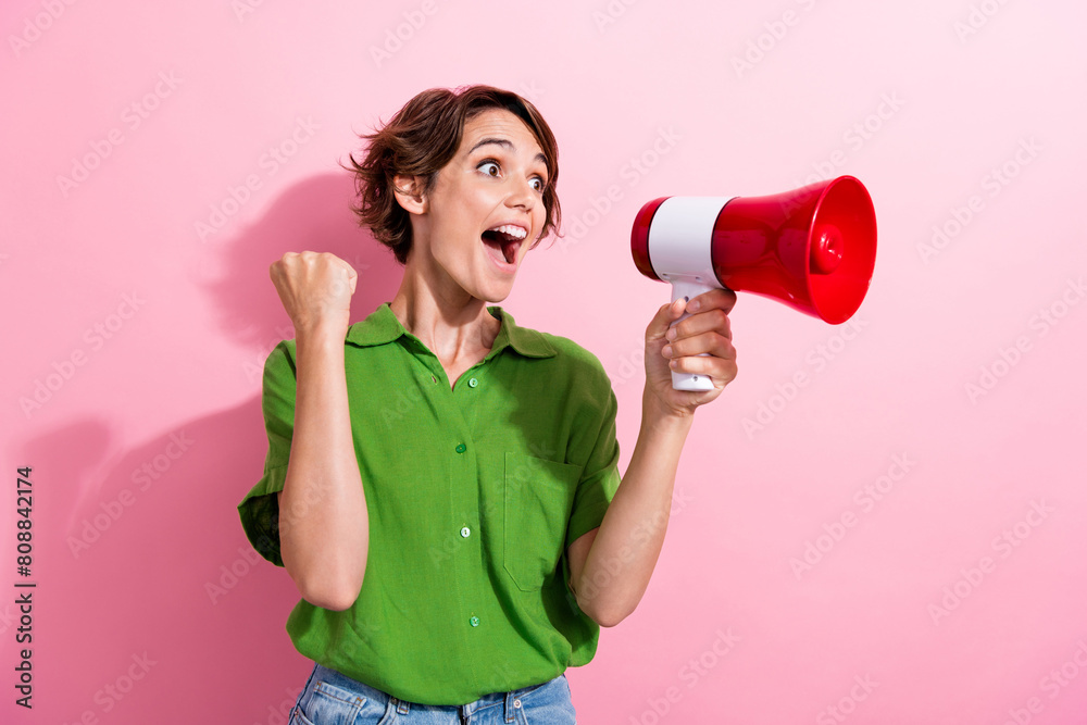 Photo portrait of pretty young girl raise fist celebrate shout megaphone wear trendy green outfit isolated on pink color background Photo portrait of pretty young girl raise fist celebrate shout megaphone wear trendy green outfit isolated on pink color background