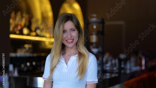 Happy young female smiling and looking at camera indoor in cafe. Beautiful Caucasian carefree blonde woman in restaurant. Positive emotions. Close up portrait. Joyful worker in bar