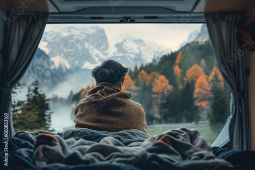 Man gazes at autumn mountains from his van, wrapped in a cozy blanket