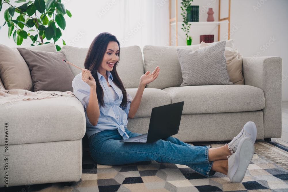 Full length portrait of pretty lady sit floor speak video call wear shirt bright interior apartment indoors Full length portrait of pretty lady sit floor speak video call wear shirt bright interior apartment indoors