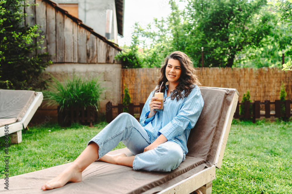 One young caucasian woman is relaxing on easy bed while drinking cold coffee in her backyard One young caucasian woman is relaxing on easy bed while drinking cold coffee in her backyard