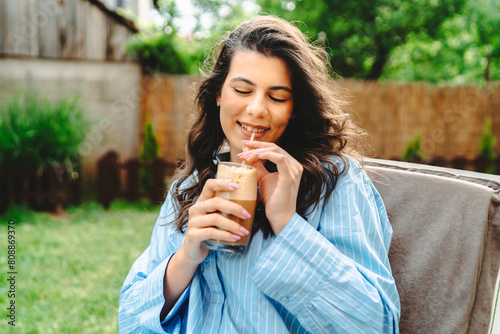 One young caucasian woman is relaxing on easy bed while drinking cold coffee in her backyard 