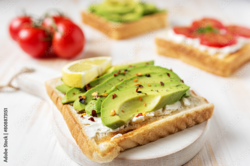 Sliced avocado on toast bread with spices on white wooden background. Food concept.
