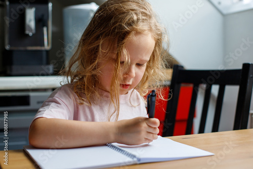 Close-up of a girl of 4s drawing in a notebook in the kitchen of the house. upbringing of children. children's leisure time. home upbringing of a child photo