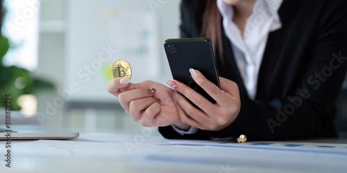 Businesswoman holding a golden bitcoin. using Mobile with graph chart, trading stock market, investing Bitcoin cryptocurrency at home office. Investment and technology concept