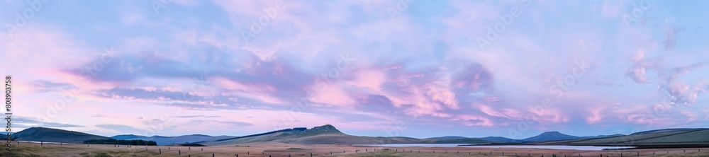 A field with mountains in the background, all under a cotton candy sky filled with clouds