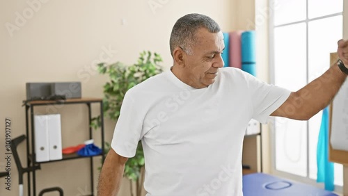 A middle-aged man flexing muscles smilingly in a healthcare rehabilitation center's bright room. photo
