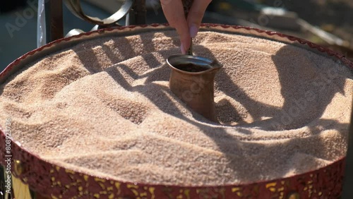 Person cooking coffee on the hot sand. A view of person hand preparing coffee on the hot sand in the city place during day time. photo