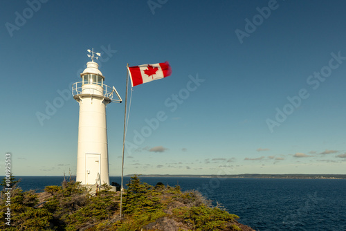 The round tower of King's Cove Lighthouse is built high on a cliff over the Atlantic with a proud  flag of Canada, King's Cove, Newfoundland photo