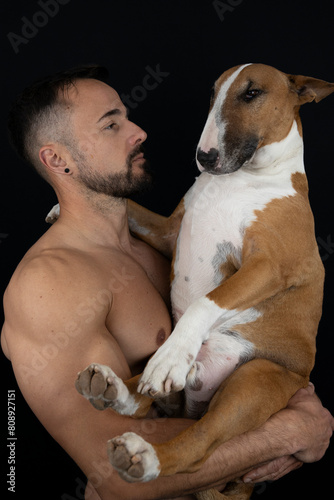 Strong shirtless man on black background hugging his dog