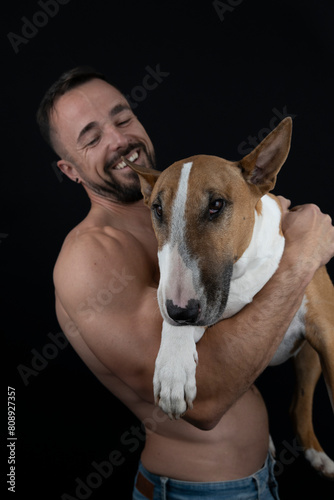 Strong shirtless man on black background hugging his dog