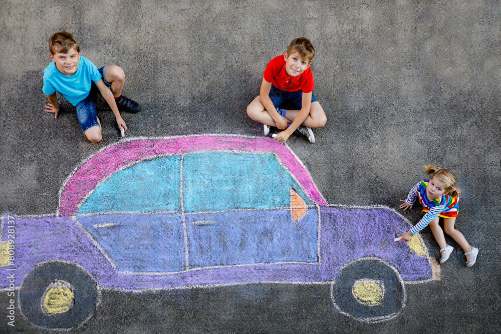 Φωτογραφία three little children, two school kids boys and toddler girl having fun with with car picture drawing with colorful chalks on asphalt