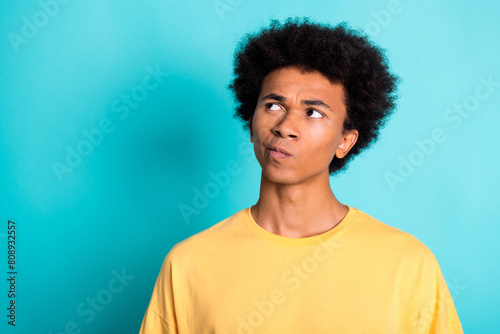 Portrait of minded puzzled man with afro hairstyle wear oversize t-shirt look at offer empty space isolated on teal color background © deagreez