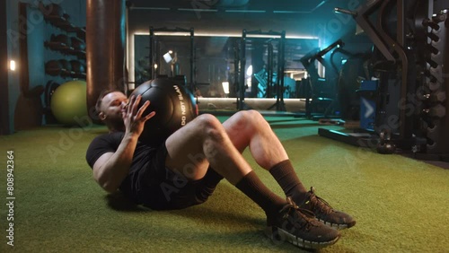 A man in sportswear is intensely working out with a medicine ball in the gym, focusing on strength training and conditioning. His dedication to fitness is evident in his vigorous exercise routine