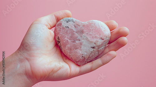 Hand Holding Pink Heart Shaped Stone on Soft Pink Background Expressing Love and Care photo