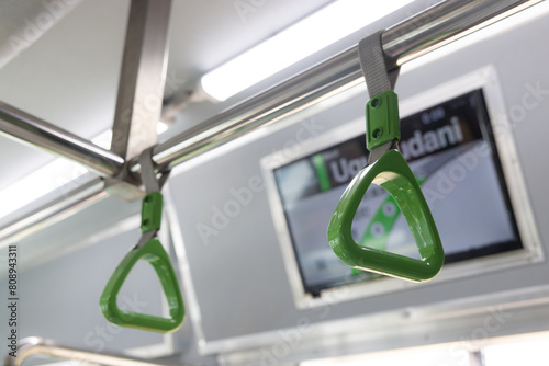 A green and silver hand rail in public train. The rail is attached to a metal pole.
