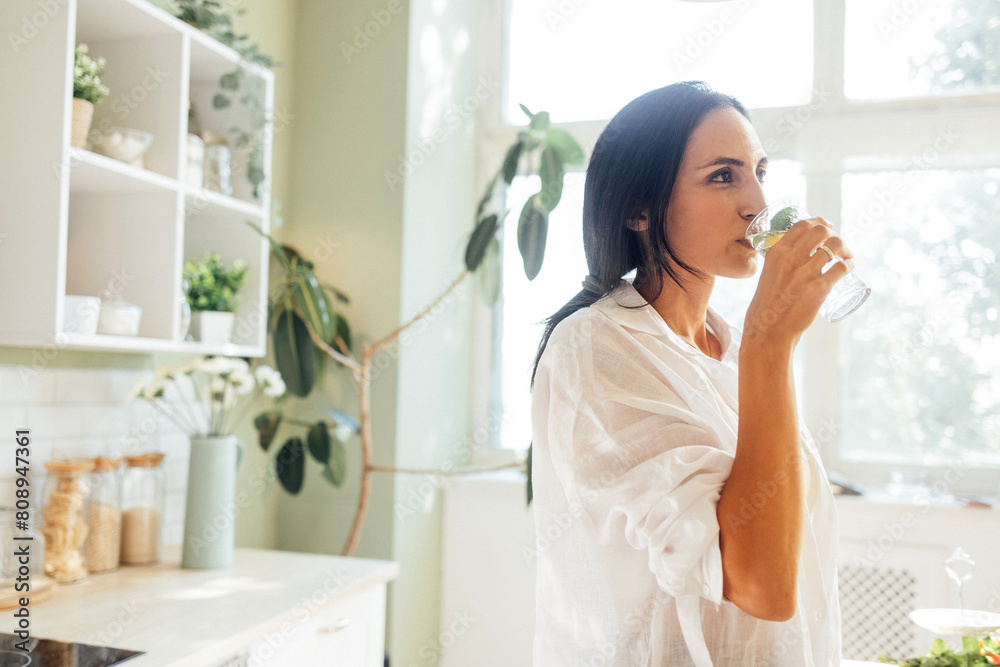 An attractive young woman is drinking fresh tasty homemade lemonade in the kitchen An attractive young woman is drinking fresh tasty homemade lemonade in the kitchen