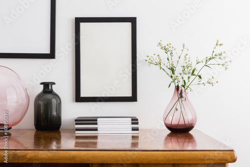 Spring flowers in a vase and black frame mock up over vintage oak desk. © mallmo