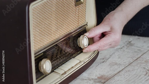 A close-up view of a woman's hand tuning the knobs on an old-fashioned radio set against a simple background, evoking a sense of nostalgia.