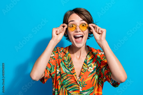 Photo of astonished positive girl arms touch sunglass open mouth cant believe isolated on blue color background