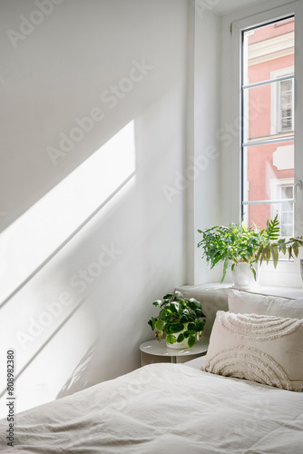 Close up of bed with bedding, side table and pot near window in room. © brizmaker